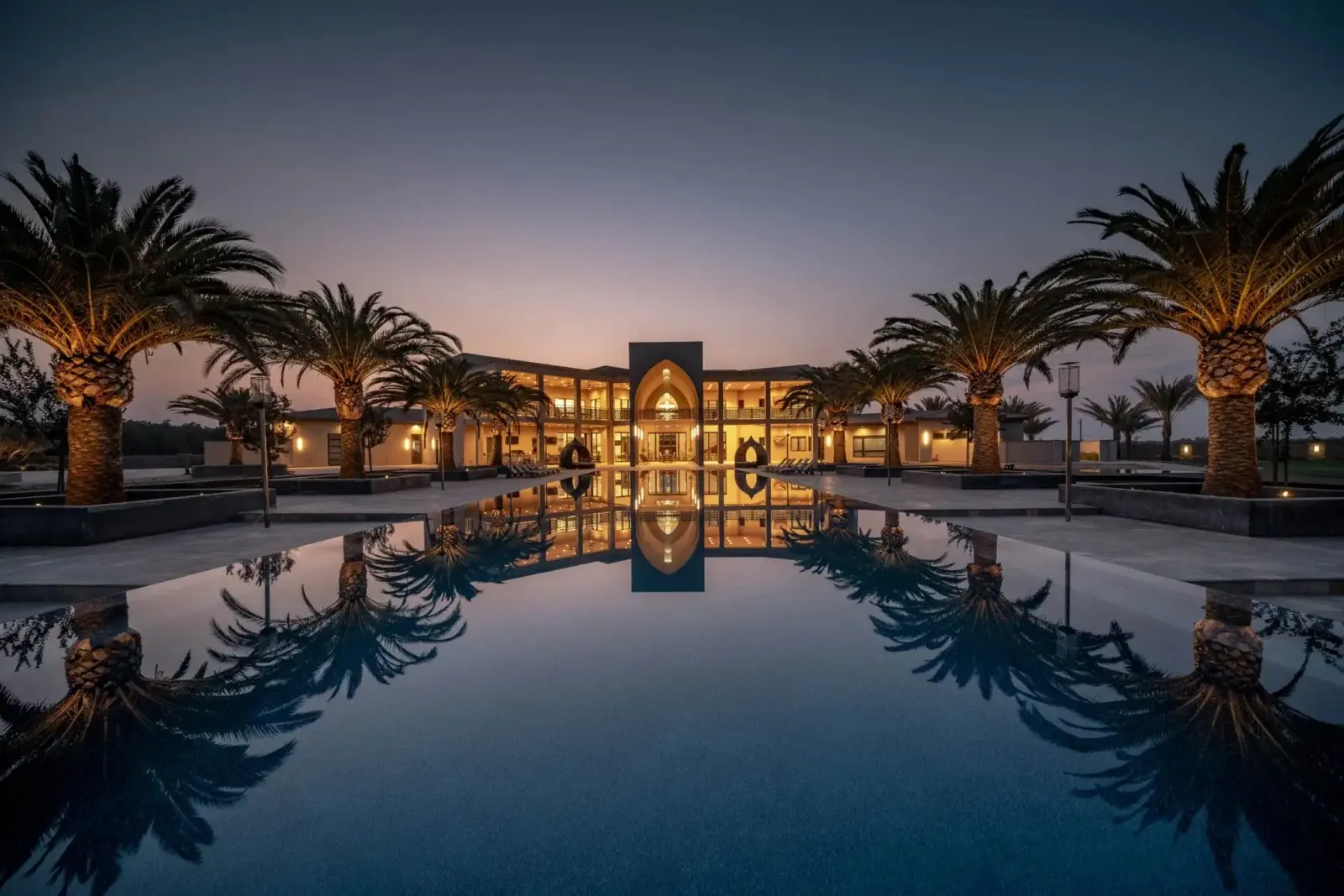 Luxury resort with palm trees and pool reflection at dusk