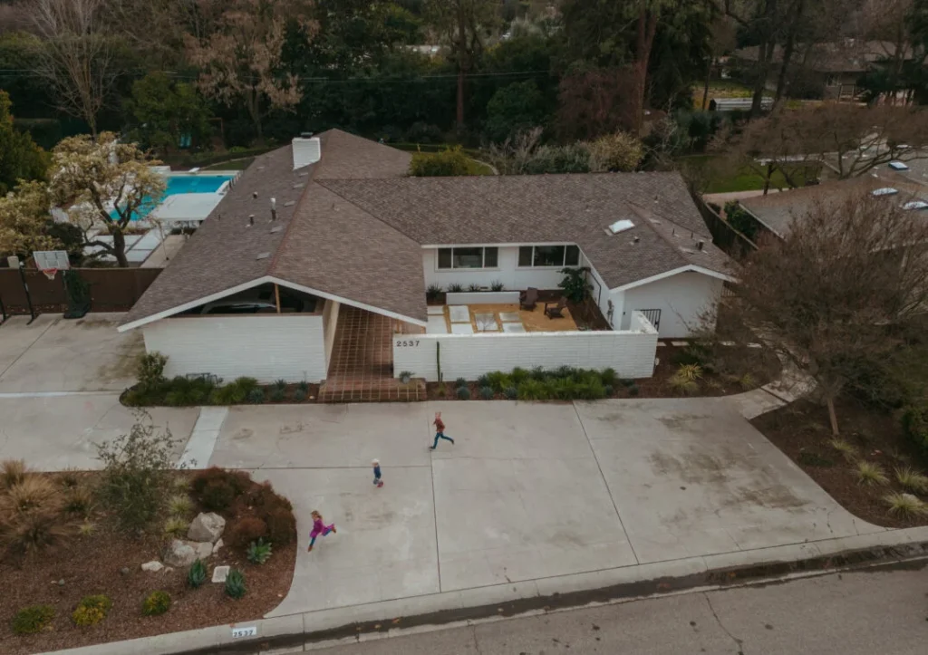 Aerial view of a suburban house with a patio, driveway, and three children running in front